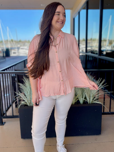 KORT IN CORAL CHEYANNE STRIPED BUTTON UP SHIRT FRONT VIEW HOLDING HEM LOOKING TO SIDE