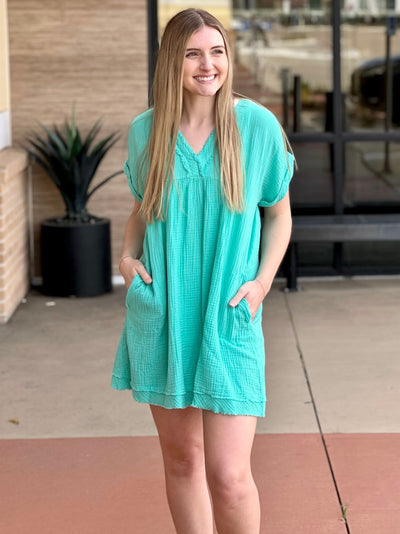 Lexi in mint dress, both hands in pockets smiling looking to the side