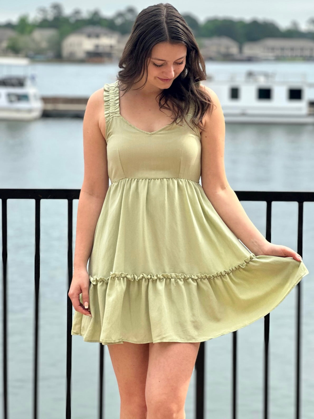 Megan in olive dress holding dress and looking down at dress