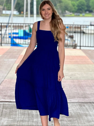 Lexi in bright blue midi dress holding dress smiling
